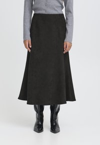 Gonna midi in camoscio nero con una silhouette svasata, dotata di dettagli in cuciture verticali. Indossata con un top grigio a maniche lunghe e stivaletti neri.