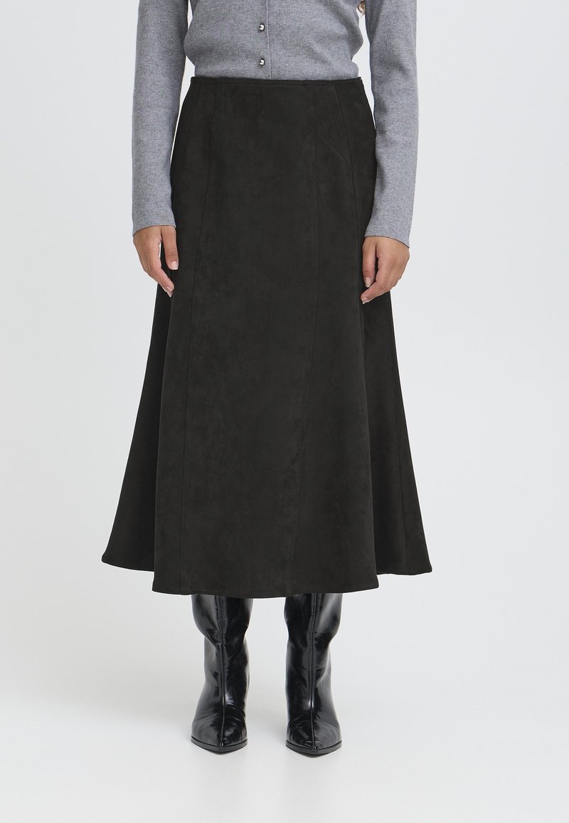 Gonna midi in camoscio nero con una silhouette svasata, dotata di dettagli in cuciture verticali. Indossata con un top grigio a maniche lunghe e stivaletti neri.