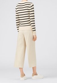 Sweter w paski z dzianiny w kolorze kremowym i czarnym, z prążkowanym obszyciem. Połączony z jasnobeżowymi spodniami o szerokich nogawkach oraz białymi sneakersami z beżowymi akcentami.