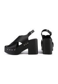 Sandales à plateforme noires avec talons épais, brides croisées à l'avant, fermetures à boucle à la cheville et détails de clous métalliques le long des bords de la semelle.