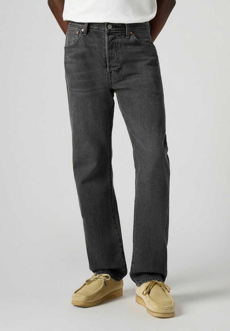 Jeans in velluto a coste neri con vestibilità dritta, caratterizzati da righe verticali e classico design a cinque tasche, abbinati a scarpe mocassino color cammello.