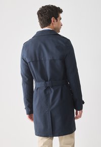 Abrigo de marinero con cintura ceñida, epaulettes en los hombros y un acabado suave y texturizado. Presenta un corte de longitud media y cuello clásico.