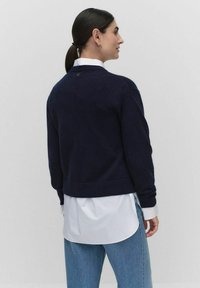 Marineblauwe korte trui van een zacht materiaal, met een ronde halslijn en geribbelde onderkant, gecombineerd met een wit overhemd eronder.