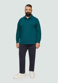 Türkisfarbenes Langarm-Polohemd mit Kragen, zwei Knöpfen und gerippten Bündchen, kombiniert mit dunkelblauen Hosen und weißen Sneakers. Glatte Textur.