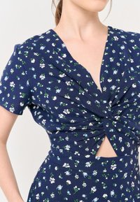 Abito navy con stampa floreale bianca e blu, maniche corte, design a torsione sul davanti e dettaglio cut-out in vita. Tessuto morbido.