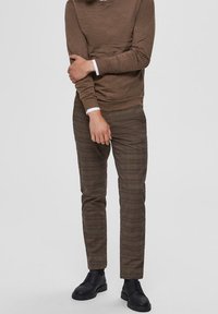 Braunes Langarmhemd kombiniert mit beige-braunen karierten Hosen. Schwarze Schnürschuhe vervollständigen das Outfit und zeichnen sich durch einen schmalen Schnitt aus.