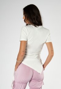 Weißes kurzärmliges T-Shirt mit abgerundetem Saum, weichem Material und tailliertem Schnitt, kombiniert mit hellrosa Cargo-Hosen mit seitlichen Taschen.