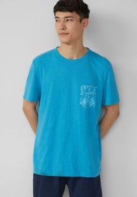 Korte mouwen t-shirt in helder teal, met een gestructureerde zak met een subtiel patroon. Zachte stof met een ontspannen pasvorm.