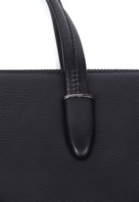Sort læder håndtaske med en glat tekstur, en struktureret form og et slankt håndtag med en sølvaccent.
