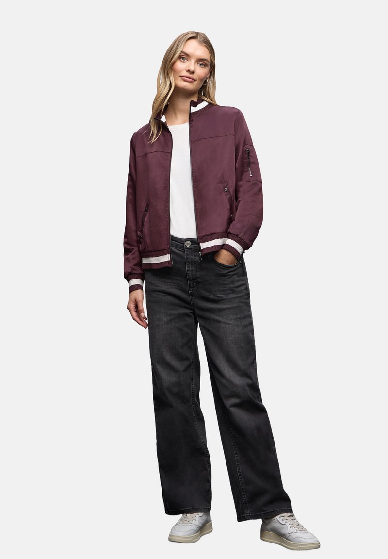 Burgundowa bomberka z ribbowymi akcentami, zestawiona z czarnymi szerokimi spodniami i jasnymi trampkami, z białym, gładkim t-shirtem pod spodem.