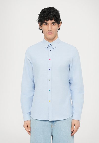 Light blue long-sleeve shirt with a collared neckline and colorful buttons down the front, paired with light denim jeans.