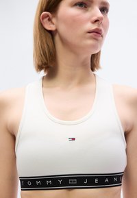 Λευκό αθλητικό τοπ με ριμπ υφή, με μικρό λογότυπο στο κέντρο και αντίθετη μαύρη ταινία που γράφει "TOMMY JEANS".