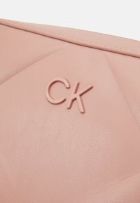 Borsa in pelle rosa con superficie testurizzata, caratterizzata da un design trapuntato e un logo 'CK' in rilievo. Le linee eleganti e la finitura morbida sono prominenti.