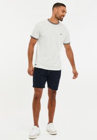 Camiseta gris de manga corta con cuello de canalé que presenta franjas rojas y marinas, combinada con pantalones cortos marinos y zapatillas blancas.