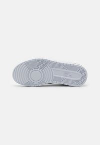 Suela de zapatilla blanca con un patrón de agarre texturizado y acentos circulares. Presenta surcos y líneas para tracción, destacando el diseño de la suela.
