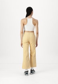 Pantaloni a zampa d'elefante in corduroy giallo con tasche posteriori, abbinati a una canotta bianca e scarpe da ginnastica nere, visti da dietro.