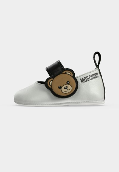 Бяло бебешко обувче с черен кант, черна каишка с кафяво мече и "Moschino" отпечатано отстрани.