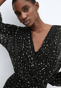 Abito nero con motivo maculato bianco, tessuto leggero, scollatura a V profonda e maniche fluide. Design minimalista con texture morbida.