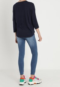 Jersey navy de gran tamaño con mangas de tres cuartos, combinado con jeans ajustados de color azul claro y zapatillas chunky multicolores con acentos florales.