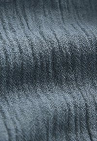 Gros plan d'un tissu tissé gris foncé froissé montrant des fils texturés et des plis en surface.