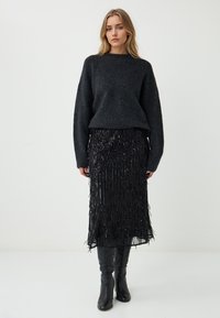 Maglione nero a maglia con colletto tondo, abbinato a una gonna a frange di paillettes nere e stivali neri al ginocchio. L'outfit presenta un design texture.