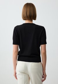 Schwarzes kurzärmliges Strickoberteil mit Rundhalsausschnitt, glatter Textur und geripptem Saum, kombiniert mit weißen maßgeschneiderten Hosen.