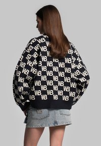 Pletený svetr v námořnické modři s krémovým geometrickým vzorem "WB". Má oversized rukávy a žebrovaný lem. Spárováno s denimovou mini sukní.