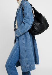 Denimová bunda v světle modré barvě, doplněná černou koženou kabelkou na rameno. Tento outfit zahrnuje béžový rolák a přiléhavé džíny.