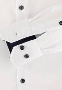 Witte gestructureerde shirt met een cutaway kraag, donkere knopen en contrasterende marineblauwe binnenmanchetten. De manchet is schuin en wordt teruggevouwen.