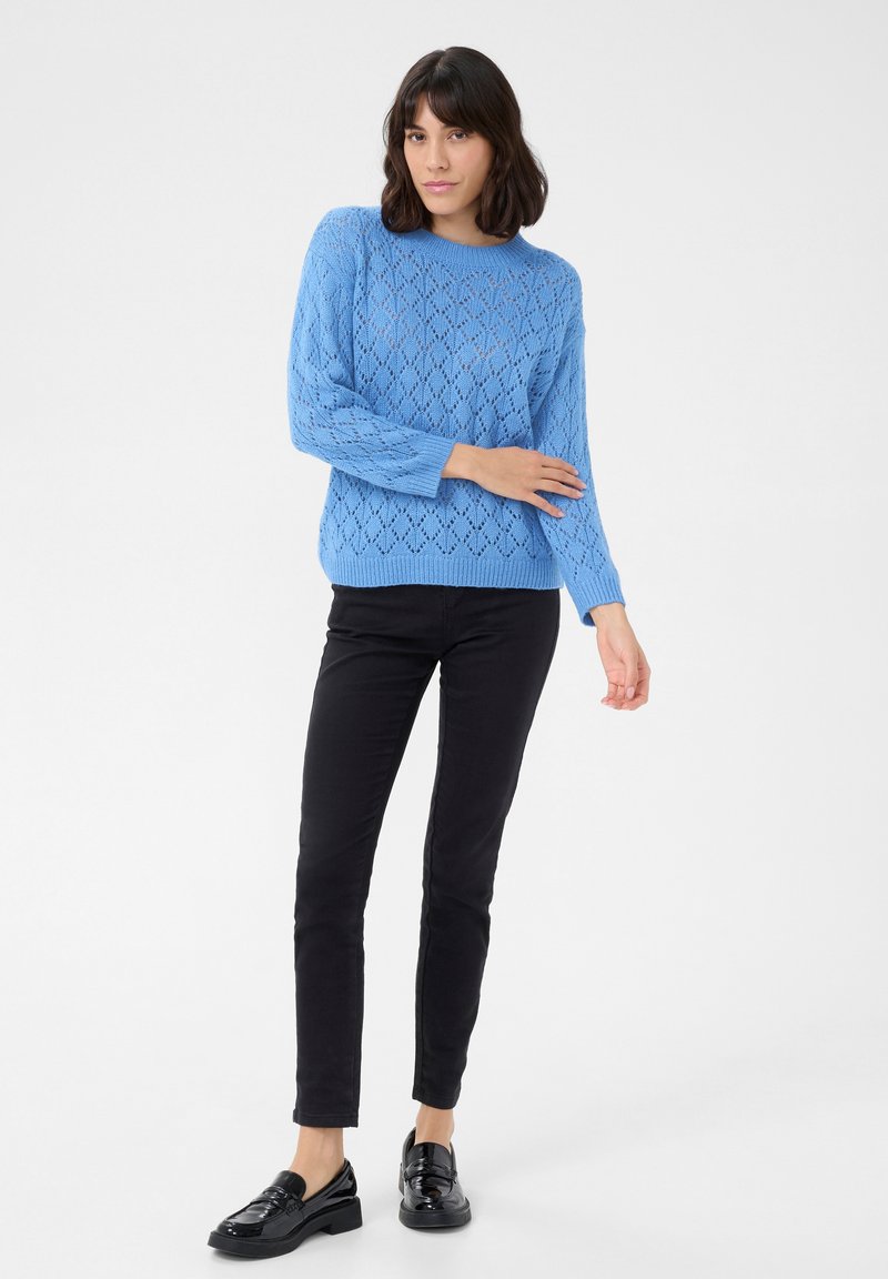 Jasnoniebieski sweter dzianinowy z wzorem w diamenty, okrągłym dekoltem i ściągaczami na rękawach, połączony z czarnymi spodniami slim fit i czarnymi mokasynami.