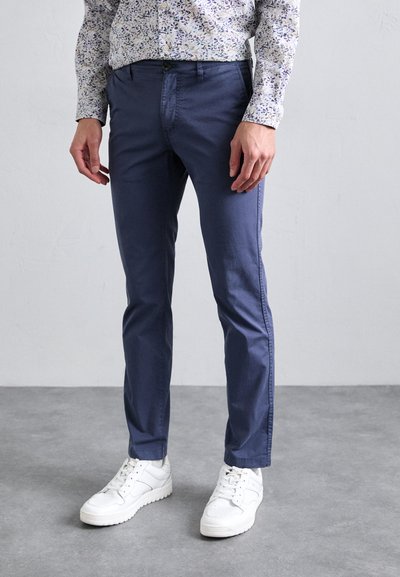 Pantaloni din bumbac de culoare bleumarin, cu o croială slim, având buzunare frontale și închidere cu nasture, asortați cu adidași albi.