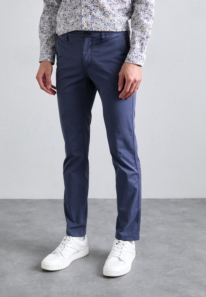 Chinos in cotone blu navy con vestibilità slim, dotati di tasche frontali e chiusura con bottone, abbinati a sneakers bianche.