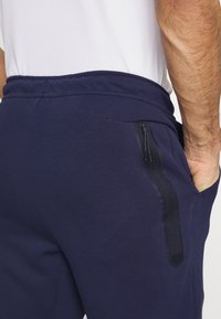 Navy jogger pants made of soft fabric with an elastic waistband, featuring a zippered pocket and a sleek, minimal design.