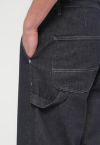 Temno modre kavbojke iz jeansa z zadnjim žepom in bočnim žepom, s subtilnim šivom, klasičnim krojem in gladko teksturo.