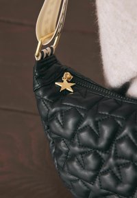Fekete steppelt kézitáska fényes textúrával, arany csillag alakú díszítéssel a cipzáron és mintás pánttal a sokoldalúság érdekében.