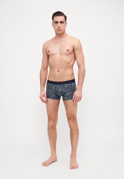 Trunks en stretch bleu marine foncé avec un motif à petites taches. Comprend une taille élastique avec logo. Texture lisse, design ajusté et longueur mi-cuisse.