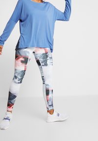 Blå långärmad topp som är kombinerad med flerfärgade leggings med abstrakta mönster. Vita sportskor fulländar outfiten.