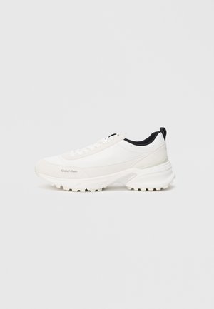 White athletic shoes with a smooth upper and padded collar, featuring a distinct textured sole for grip and subtle branding on the side.