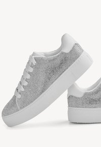 Sølv sneakers med en teksturert, glitrende overdel og hvit gummisåle. Har flate lisser og en rund tådesign.