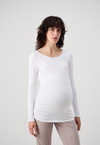 Long-sleeve, fitted maternity top in white, made of smooth fabric, featuring a scoop neckline and stretchy design to accommodate a growing belly.