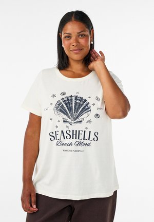 Frau mit glatten dunklen Haaren, die ein weißes T-Shirt mit einer großen Muschel und dem Schriftzug „Seashells Beach Mood“ trägt.