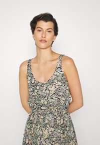 Vestido floral com decote arredondado, apresentando um fundo preto e padrões de flores em rosa claro, amarelo e verde. Tecido leve.