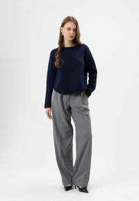 Navy knit sweater with a round neckline, paired with light gray wide-leg trousers. Shoes are black pointed heels. Smooth texture throughout.