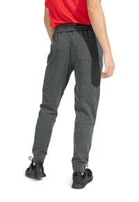 Graue Jogginghose mit strukturiertem Muster, elastischem Bund und zwei Gesäßtaschen, kombiniert mit schwarzen Sneakers.