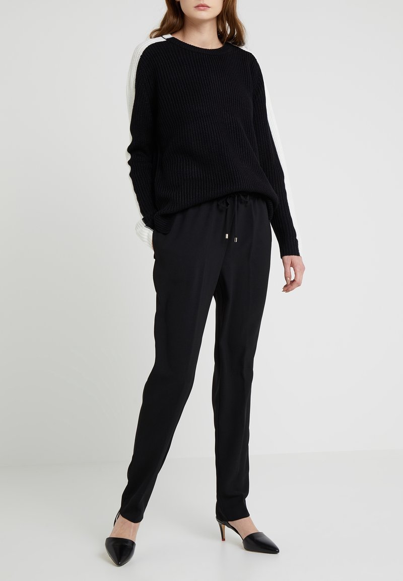 Pull noir en maille côtelée avec des détails blancs sur les manches, associé à un pantalon noir ajusté et des talons noirs pointus.