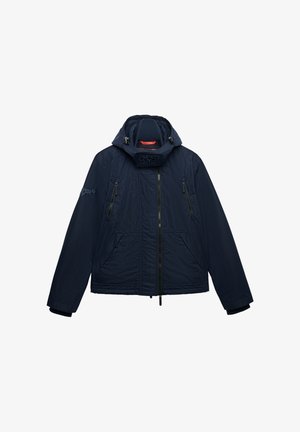 Marineblauw gewatteerd jack met capuchon, ritssluiting aan de voorkant, twee borstzakken met rits, twee lagere zakken met klep en een merklogo op de linkermouw en de nekflap.