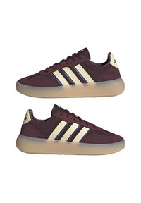 Bordo atletske tenisice s kremastim tri prugama, teksturirani materijal i prozirna potplata. Glatka gornja površina i podstavljena ovratnik za udobnost.