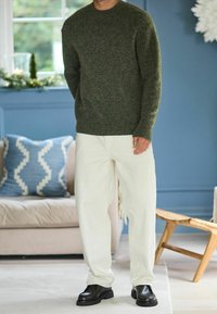 Green knitted sweater with a round neckline, paired with off-white loose-fit pants and black chunky shoes. Notable texture and color contrast.