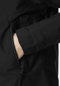 Chaqueta negra con un bolsillo con cremallera en el lado izquierdo. Textura de tela suave con mangas con puños y un discreto detalle en el hardware.