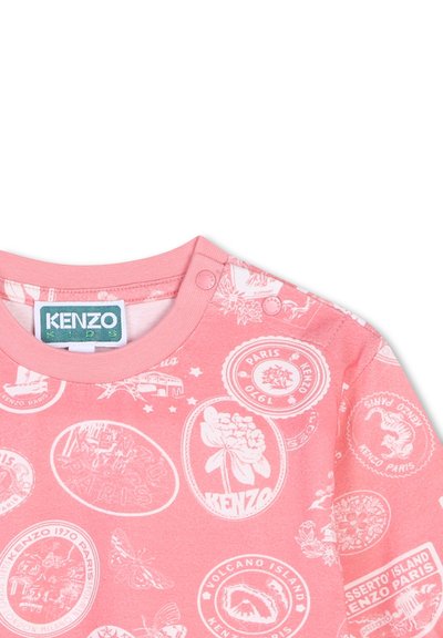 Chemise rose à manches courtes ornée d'un motif blanc de timbres et de logos, avec un col côtelé et des boutons-pression à l'épaule.